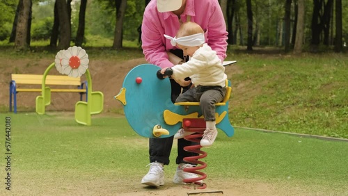 Mother swings her child on spring riders on playground in the park outdoors