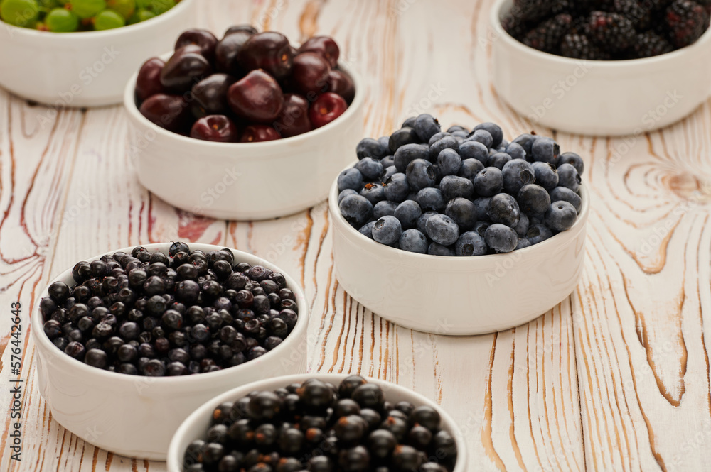 Ripe blueberries on the table in a plate, among the assortment of ripe berries, raspberries, blueberries, gooseberries, currants, shot close-up Ripe blueberries on the table in a plate, among the assortment of ripe berries, raspberries, blueberries, gooseberries, currants, shot close-up