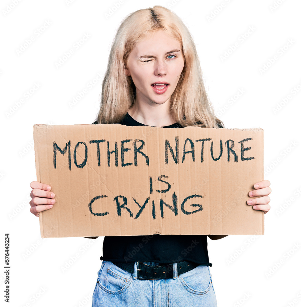 Young caucasian woman holding mother nature is crying protest cardboard banner winking looking at the camera with sexy expression, cheerful and happy face. Young caucasian woman holding mother nature is crying protest cardboard banner winking looking at the camera with sexy expression, cheerful and happy face.