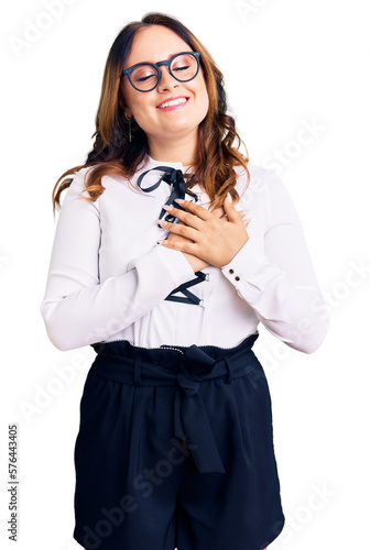 Young beautiful caucasian woman wearing business shirt and glasses smiling with hands on chest with closed eyes and grateful gesture on face. health concept.