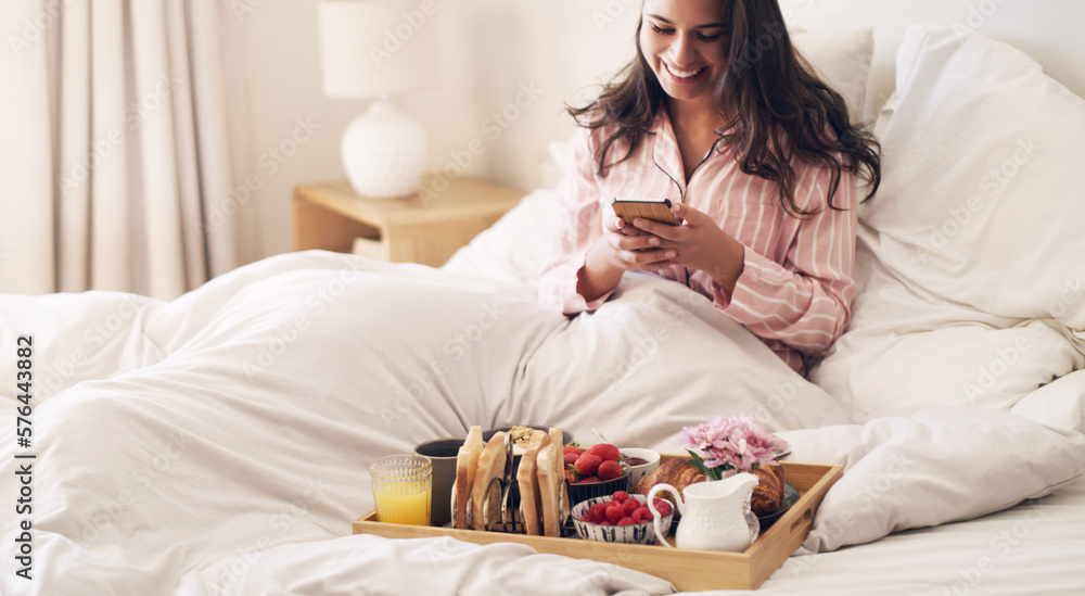 The best way to start the day. Shot of a beautiful young woman using a smartphone while having breakfast in bed at home. The best way to start the day. Shot of a beautiful young woman using a smartphone while having breakfast in bed at home.