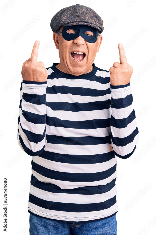 Senior handsome man wearing burglar mask and t-shirt showing middle finger doing fuck you bad expression, provocation and rude attitude. screaming excited Senior handsome man wearing burglar mask and t-shirt showing middle finger doing fuck you bad expression, provocation and rude attitude. screaming excited