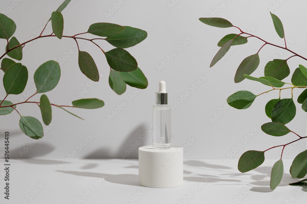 Facial serum in dropper bottle on white round podium and green eucalyptus branches on light grey background. Natural skin care cosmetic mockup. Eco beauty product for branding. Sale or presentation. Facial serum in dropper bottle on white round podium and green eucalyptus branches on light grey background. Natural skin care cosmetic mockup. Eco beauty product for branding. Sale or presentation.