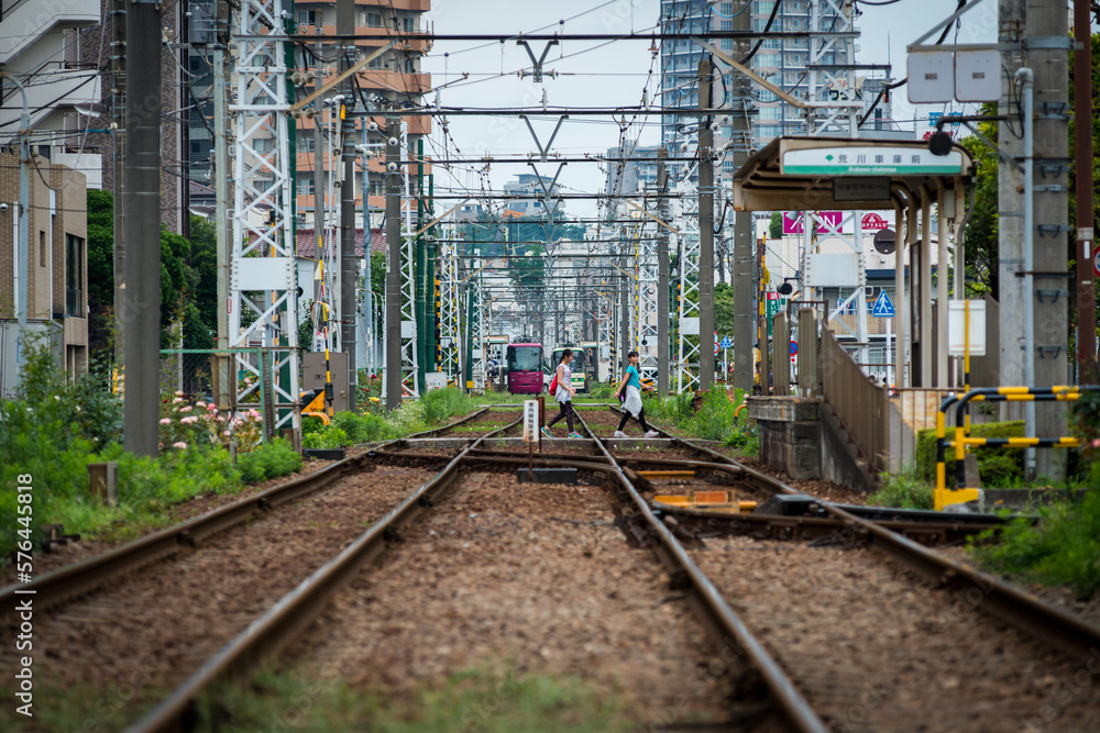 Tokyo Shitamachi trolly train (Toden) running in middle of city and two young asian girls walking across the tracks. Tokyo Shitamachi trolly train (Toden) running in middle of city and two young asian girls walking across the tracks.