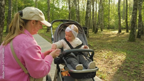 Mom feeds her child a snack in the park outdoors, mother in the park with her little daughter in a baby carriage