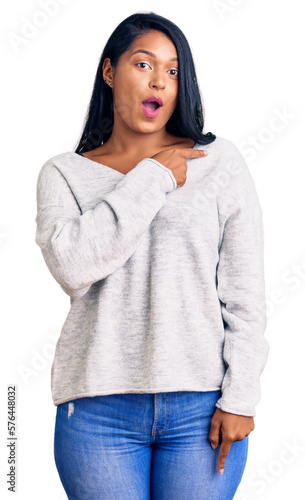 Hispanic woman with long hair wearing casual clothes surprised pointing with finger to the side, open mouth amazed expression.