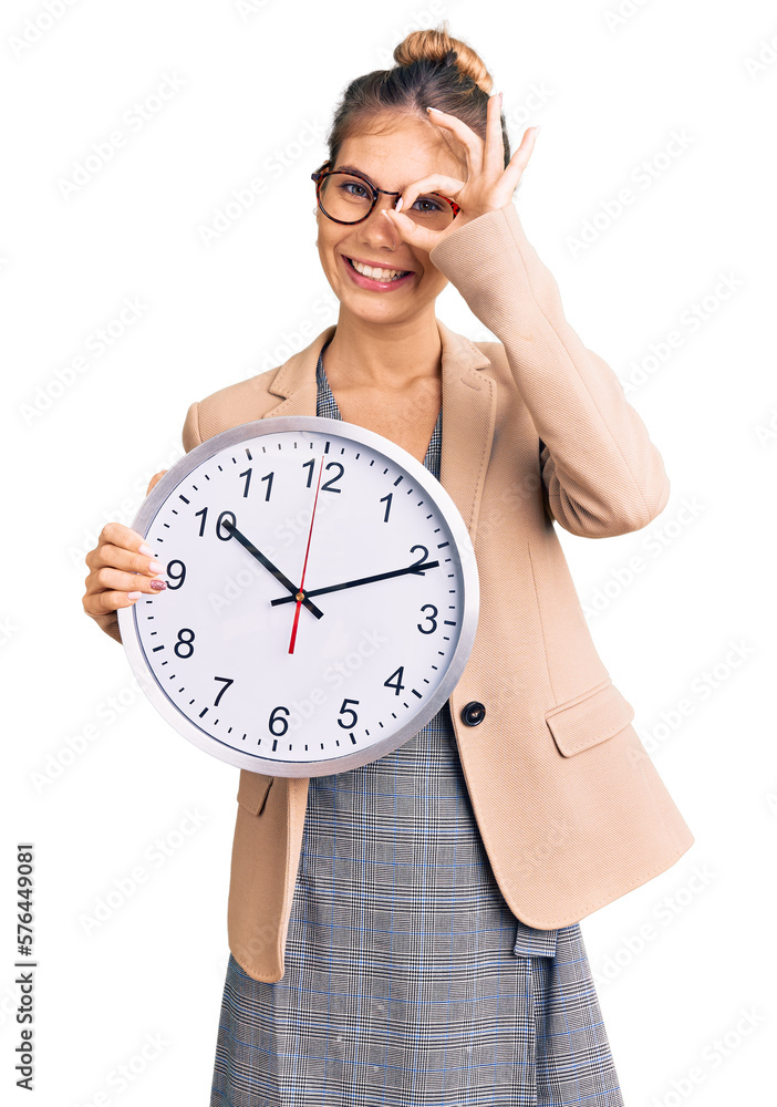Beautiful caucasian woman with blonde hair wearing business jacket and holding clock smiling happy doing ok sign with hand on eye looking through fingers
