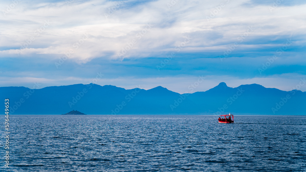 Red boat sailing on the lake towards a distant island between mountains