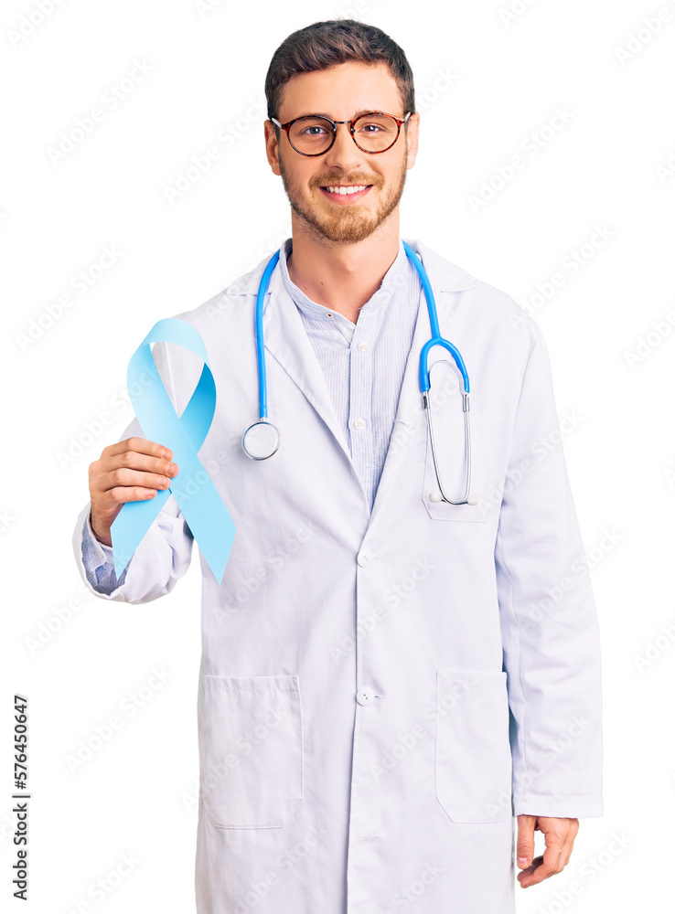 Handsome young man with bear wearing doctor uniform and holding blue ribbon looking positive and happy standing and smiling with a confident smile showing teeth Handsome young man with bear wearing doctor uniform and holding blue ribbon looking positive and happy standing and smiling with a confident smile showing teeth