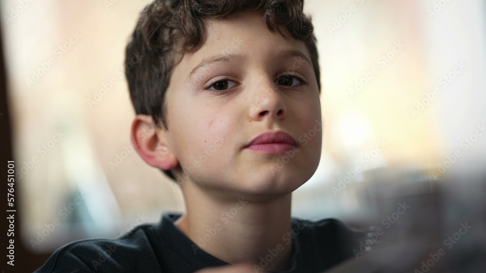 One small boy chewing food at lunch table. Candid closeup face of preteen kid eating meal. Contemplative expression One small boy chewing food at lunch table. Candid closeup face of preteen kid eating meal. Contemplative expression