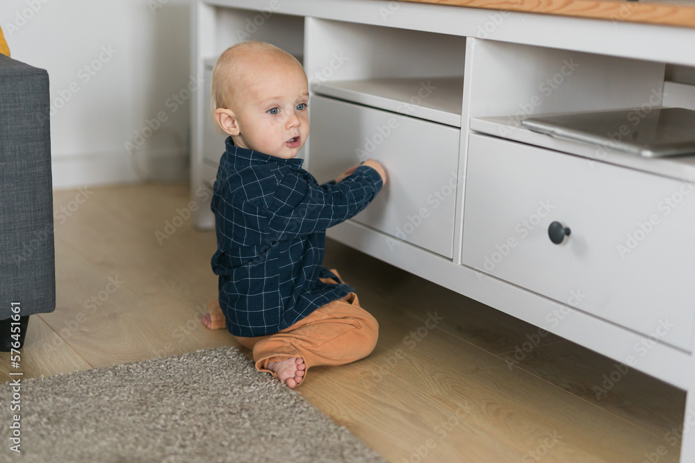 Toddler baby boy open cabinet drawer with his hand. Child explore what is in cabinet. Baby curiosity and child development stages Toddler baby boy open cabinet drawer with his hand. Child explore what is in cabinet. Baby curiosity and child development stages