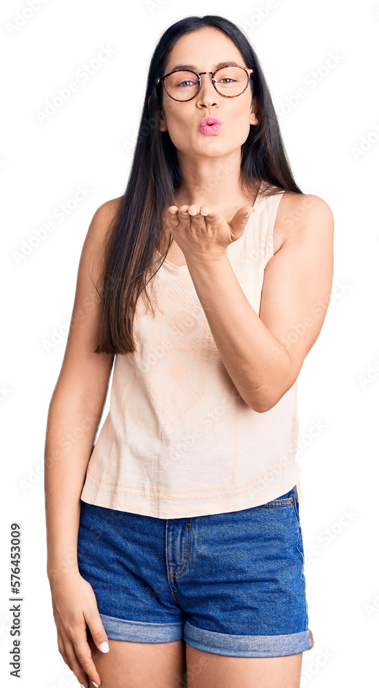 Young beautiful caucasian woman wearing casual clothes and glasses looking at the camera blowing a kiss with hand on air being lovely and sexy. love expression. Young beautiful caucasian woman wearing casual clothes and glasses looking at the camera blowing a kiss with hand on air being lovely and sexy. love expression.