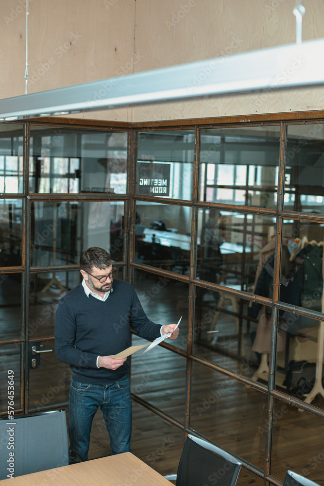 Manager holding documents, reading report, standing near office desk