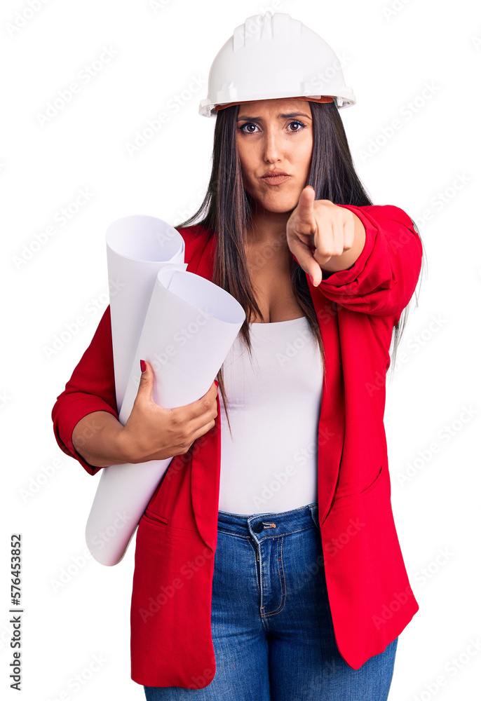 Young beautiful brunette woman wearing hardhat holding architect blueprint pointing with finger to the camera and to you, confident gesture looking serious Young beautiful brunette woman wearing hardhat holding architect blueprint pointing with finger to the camera and to you, confident gesture looking serious
