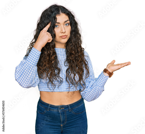 Young hispanic girl wearing casual clothes confused and annoyed with open palm showing copy space and pointing finger to forehead. think about it.