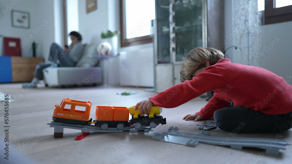 Child playing with railroad train toy at modern home living room floor. Little boy plays by himself with gift toys Child playing with railroad train toy at modern home living room floor. Little boy plays by himself with gift toys
