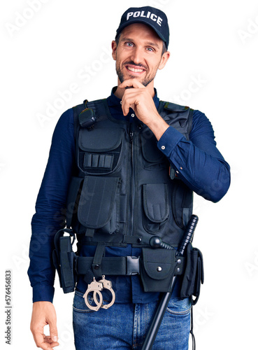 Young handsome man wearing police uniform looking confident at the camera smiling with crossed arms and hand raised on chin. thinking positive.