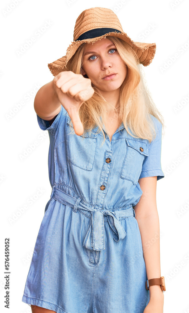 Young beautiful blonde woman wearing summer hat and dress looking unhappy and angry showing rejection and negative with thumbs down gesture. bad expression. Young beautiful blonde woman wearing summer hat and dress looking unhappy and angry showing rejection and negative with thumbs down gesture. bad expression.