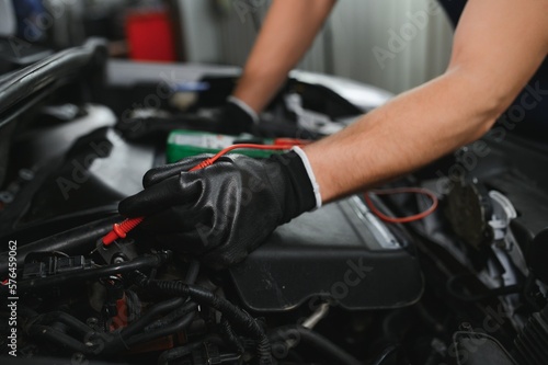 Car mechanic is using a multimeter with voltage range measurement to check the voltage level of the car battery.