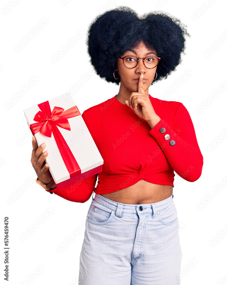 Young african american girl holding gift asking to be quiet with finger on lips. silence and secret concept. Young african american girl holding gift asking to be quiet with finger on lips. silence and secret concept.