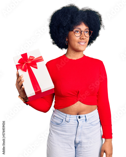 Young african american girl holding gift smiling looking to the side and staring away thinking.