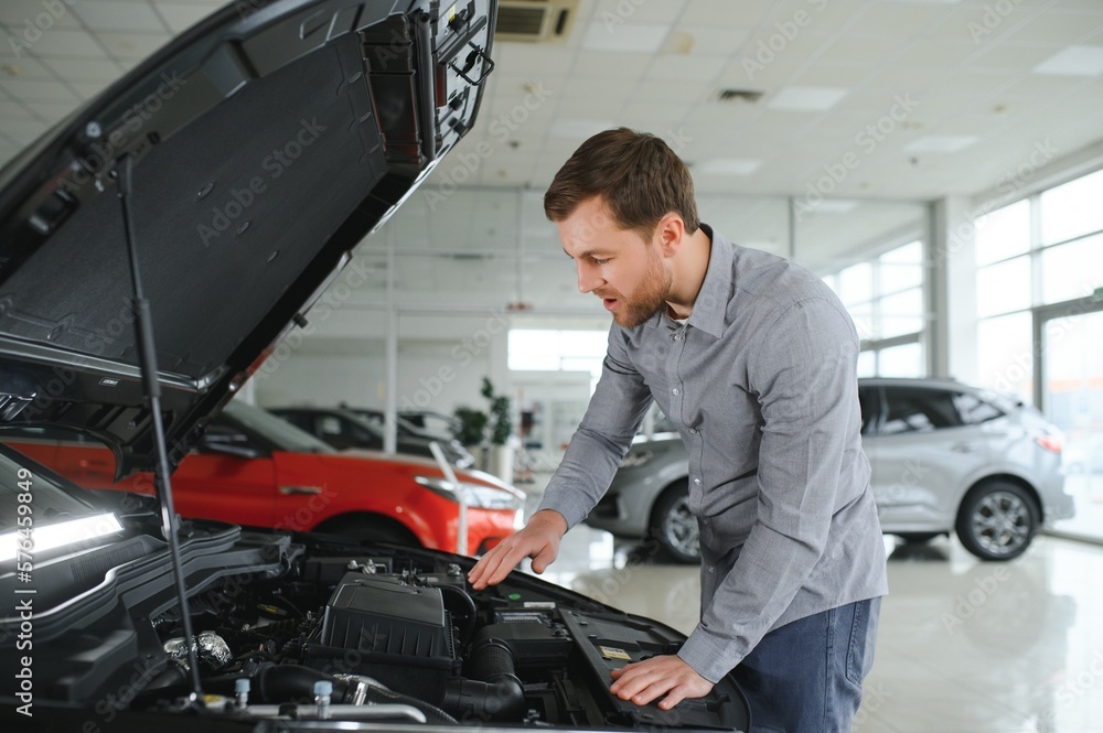 Looks under the hood of automobile. Young man in the car dealership. Looks under the hood of automobile. Young man in the car dealership.