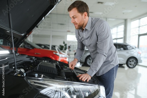 Looks under the hood of automobile. Young man in the car dealership.