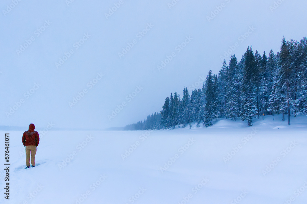 Man standing in snow-covered frozen river lined with coniferous trees in lapland