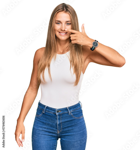 Young blonde woman wearing casual style with sleeveless shirt pointing with hand finger to face and nose, smiling cheerful. beauty concept