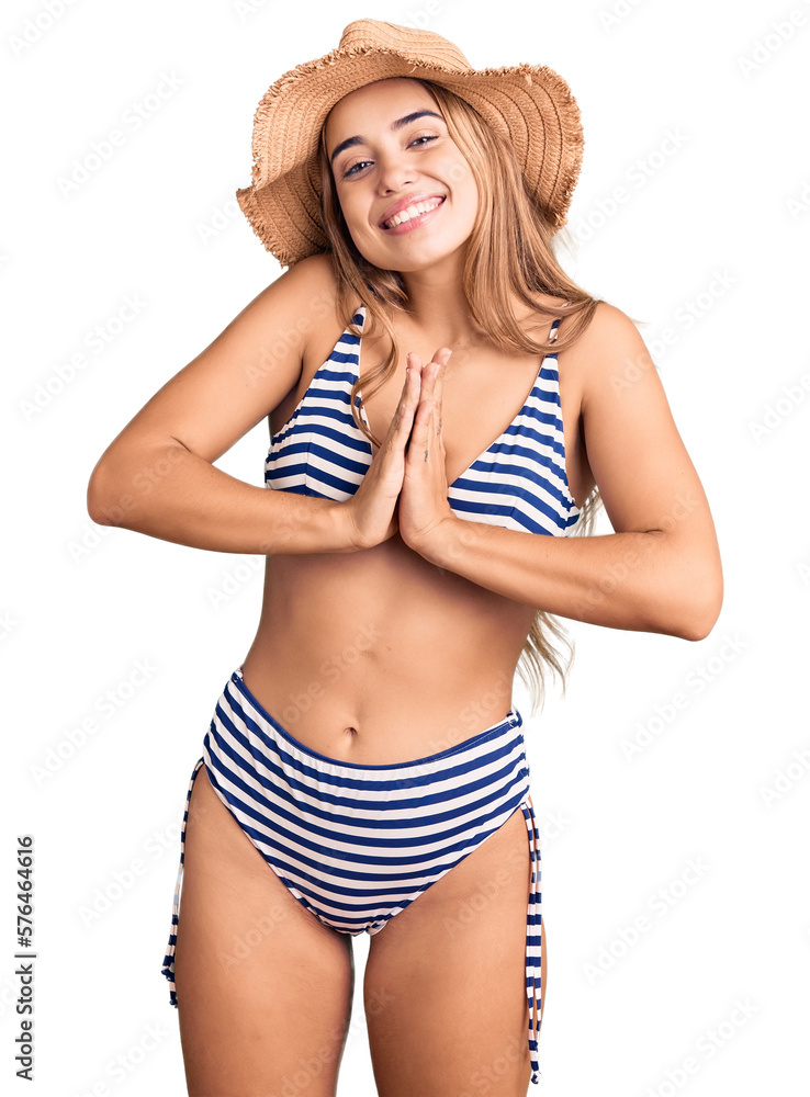 Young beautiful blonde woman wearing bikini and hat praying with hands together asking for forgiveness smiling confident. Young beautiful blonde woman wearing bikini and hat praying with hands together asking for forgiveness smiling confident.