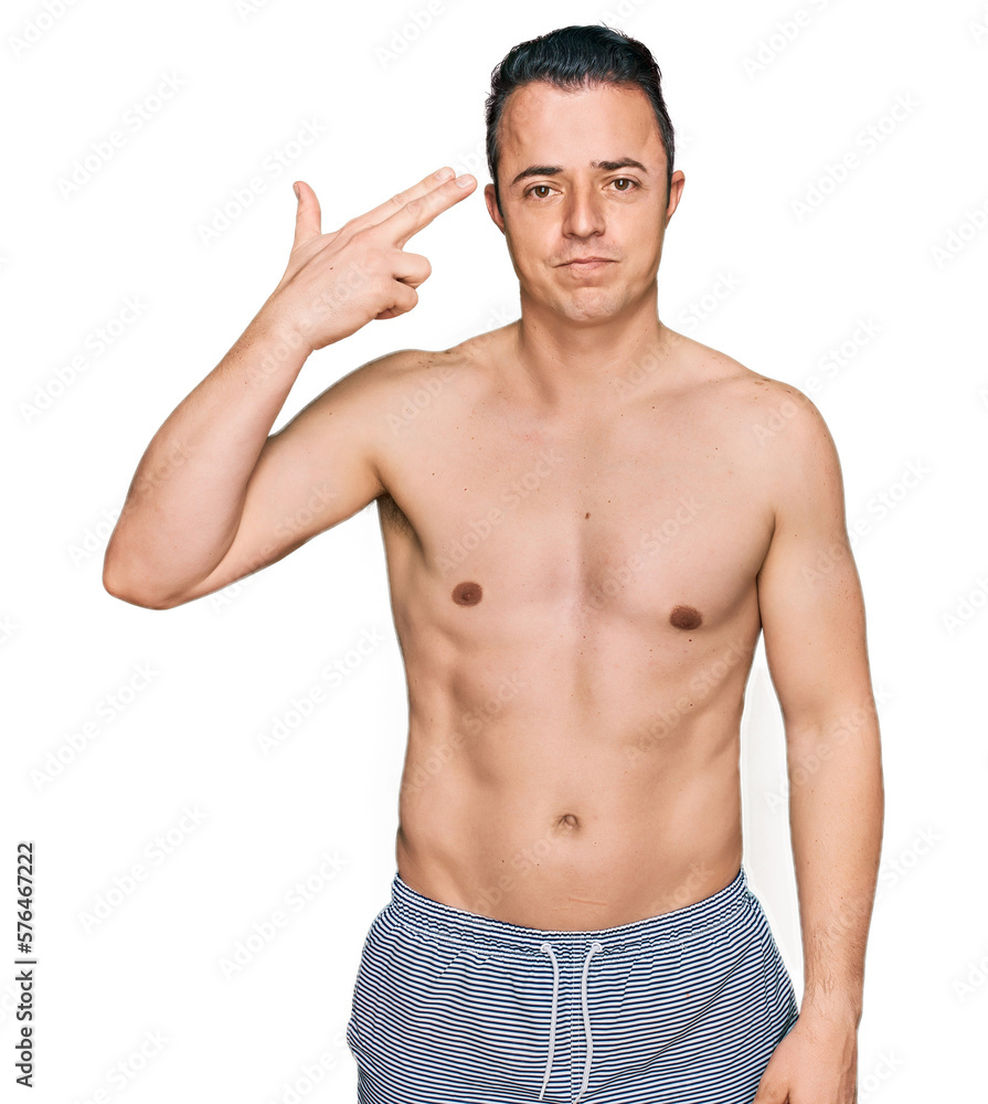 Fototapeta premium Handsome young man wearing swimwear shirtless shooting and killing oneself pointing hand and fingers to head like gun, suicide gesture.