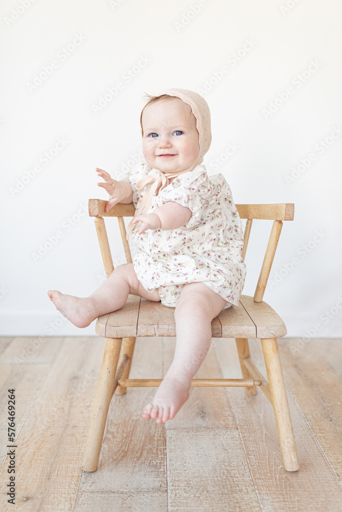 baby with a limb difference disability sitting in a wooden chair with a bonnet and floral dress baby with a limb difference disability sitting in a wooden chair with a bonnet and floral dress