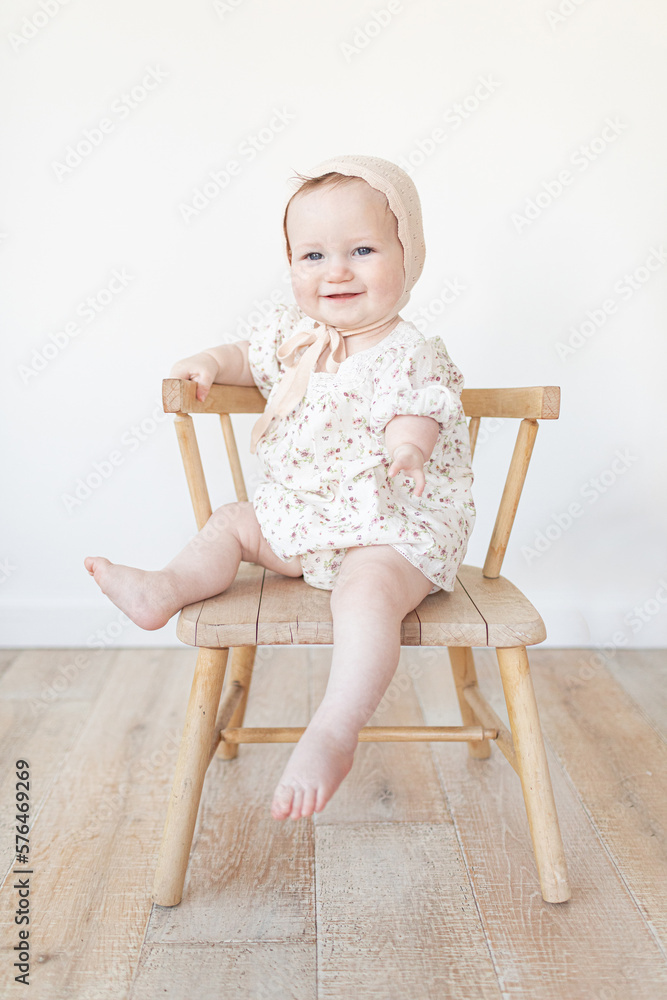 baby with a limb difference disability sitting in a wooden chair with a bonnet and floral dress baby with a limb difference disability sitting in a wooden chair with a bonnet and floral dress