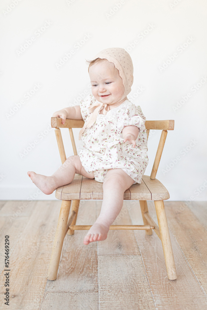 baby with a limb difference disability sitting in a wooden chair with a bonnet and floral dress baby with a limb difference disability sitting in a wooden chair with a bonnet and floral dress