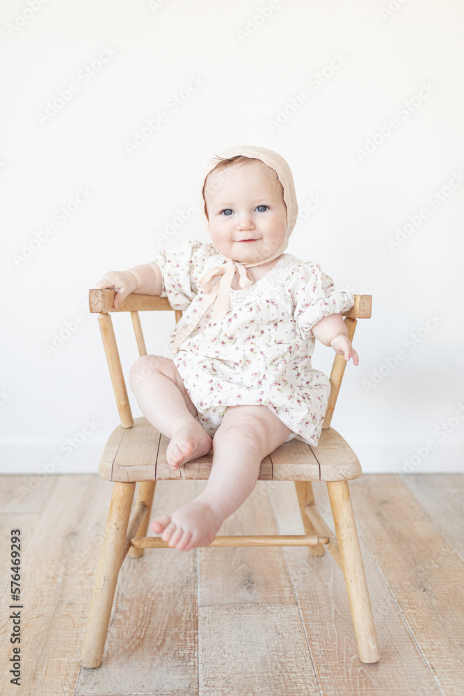baby with a limb difference disability sitting in a wooden chair with a bonnet and floral dress baby with a limb difference disability sitting in a wooden chair with a bonnet and floral dress