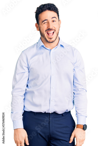 Young hispanic man wearing business clothes winking looking at the camera with sexy expression, cheerful and happy face.