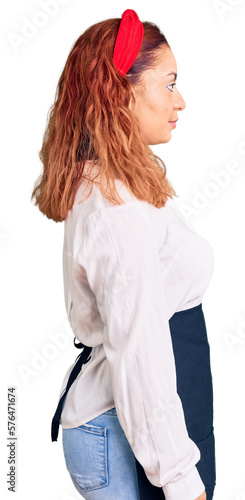 Young latin woman wearing waitress apron looking to side, relax profile pose with natural face with confident smile.