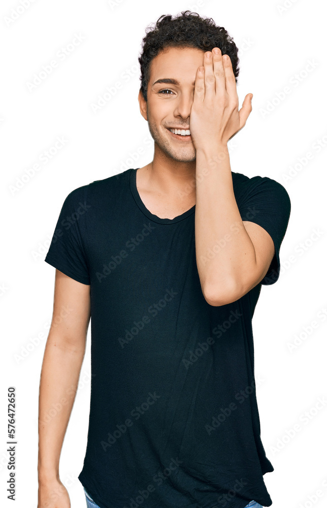Young handsome man wearing casual black t shirt covering one eye with hand, confident smile on face and surprise emotion. Young handsome man wearing casual black t shirt covering one eye with hand, confident smile on face and surprise emotion.