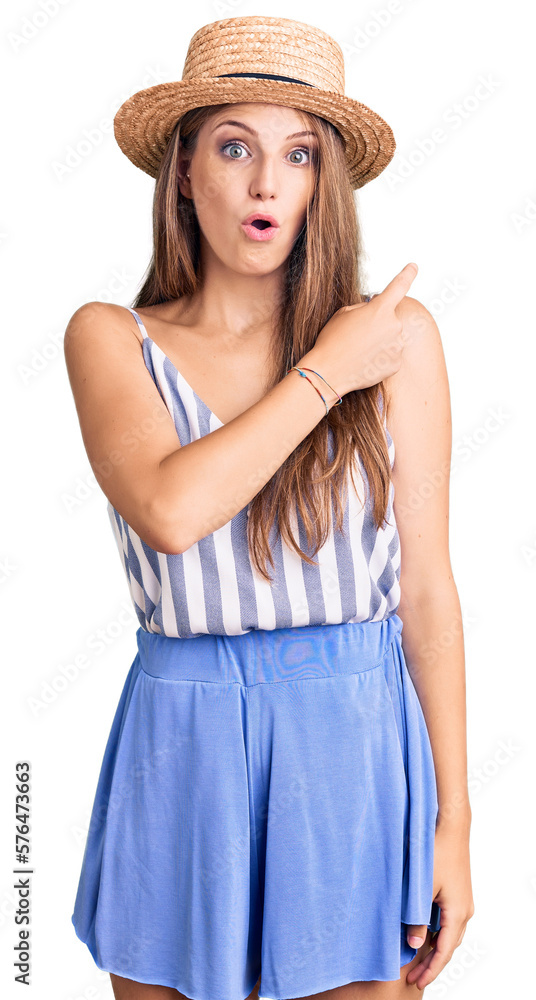 Young beautiful blonde woman wearing summer hat surprised pointing with finger to the side, open mouth amazed expression. Young beautiful blonde woman wearing summer hat surprised pointing with finger to the side, open mouth amazed expression.