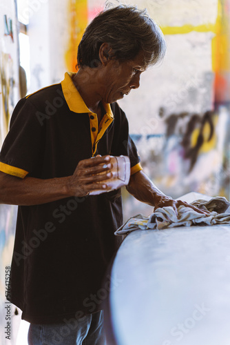 Craftsman surfboard working in a repair workshop, man spray painting a surfboard.