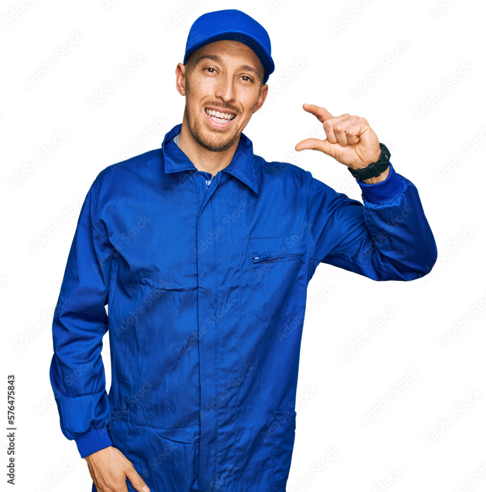 Bald man with beard wearing builder jumpsuit uniform smiling and confident gesturing with hand doing small size sign with fingers looking and the camera. measure concept.