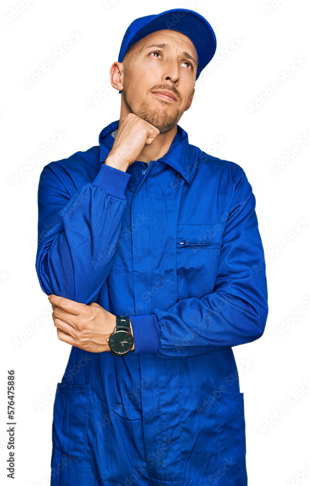 Bald man with beard wearing builder jumpsuit uniform with hand on chin thinking about question, pensive expression. smiling and thoughtful face. doubt concept. Bald man with beard wearing builder jumpsuit uniform with hand on chin thinking about question, pensive expression. smiling and thoughtful face. doubt concept.