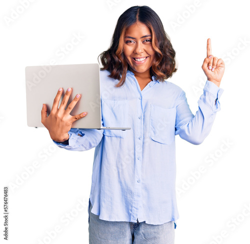 Young beautiful mixed race woman working using computer laptop surprised with an idea or question pointing finger with happy face, number one