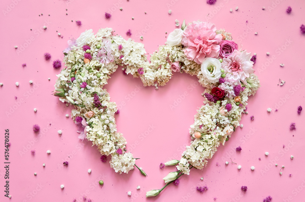 White pastel hydrangea flowers petals in heart shape on pink romantic floral background. Mothers and valentine day, wedding bridal invitations, love trendy greeting card. Top view, flat lay from above