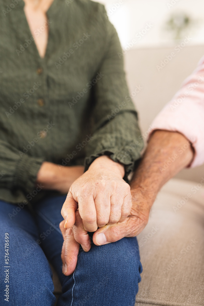 Midsection of senior diverse couple sitting on sofa and holding hands Midsection of senior diverse couple sitting on sofa and holding hands