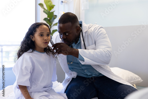 African american male doctor treating ear of biracial girl in hospital photo