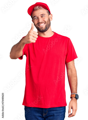 Young handsome blond man wearing t-shirt and cap doing happy thumbs up gesture with hand. approving expression looking at the camera showing success.