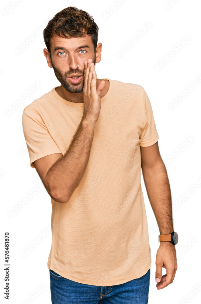 Handsome young man with beard wearing casual tshirt hand on mouth telling secret rumor, whispering malicious talk conversation Handsome young man with beard wearing casual tshirt hand on mouth telling secret rumor, whispering malicious talk conversation
