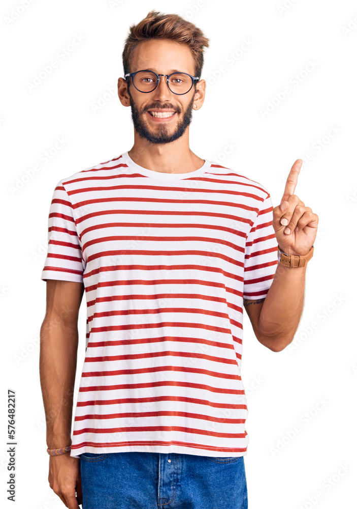 Handsome blond man with beard wearing casual clothes and glasses with a big smile on face, pointing with hand finger to the side looking at the camera. Handsome blond man with beard wearing casual clothes and glasses with a big smile on face, pointing with hand finger to the side looking at the camera.