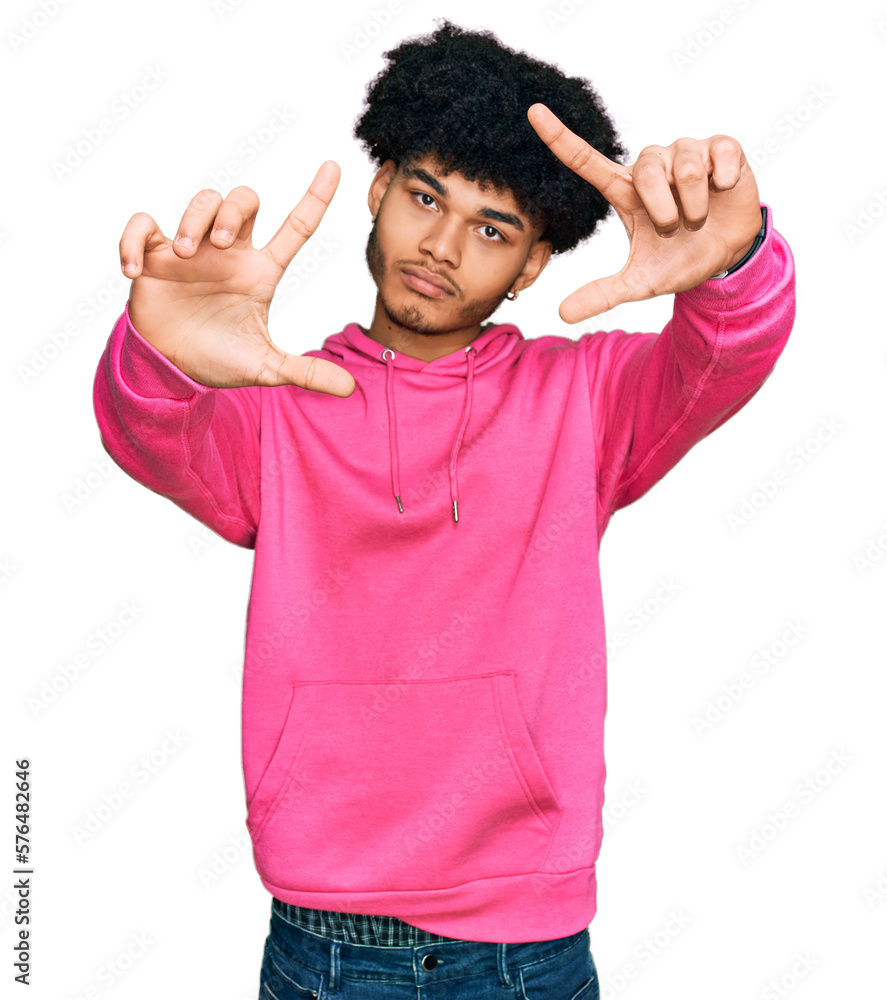 Young african american man with afro hair wearing casual pink sweatshirt doing frame using hands palms and fingers, camera perspective Young african american man with afro hair wearing casual pink sweatshirt doing frame using hands palms and fingers, camera perspective